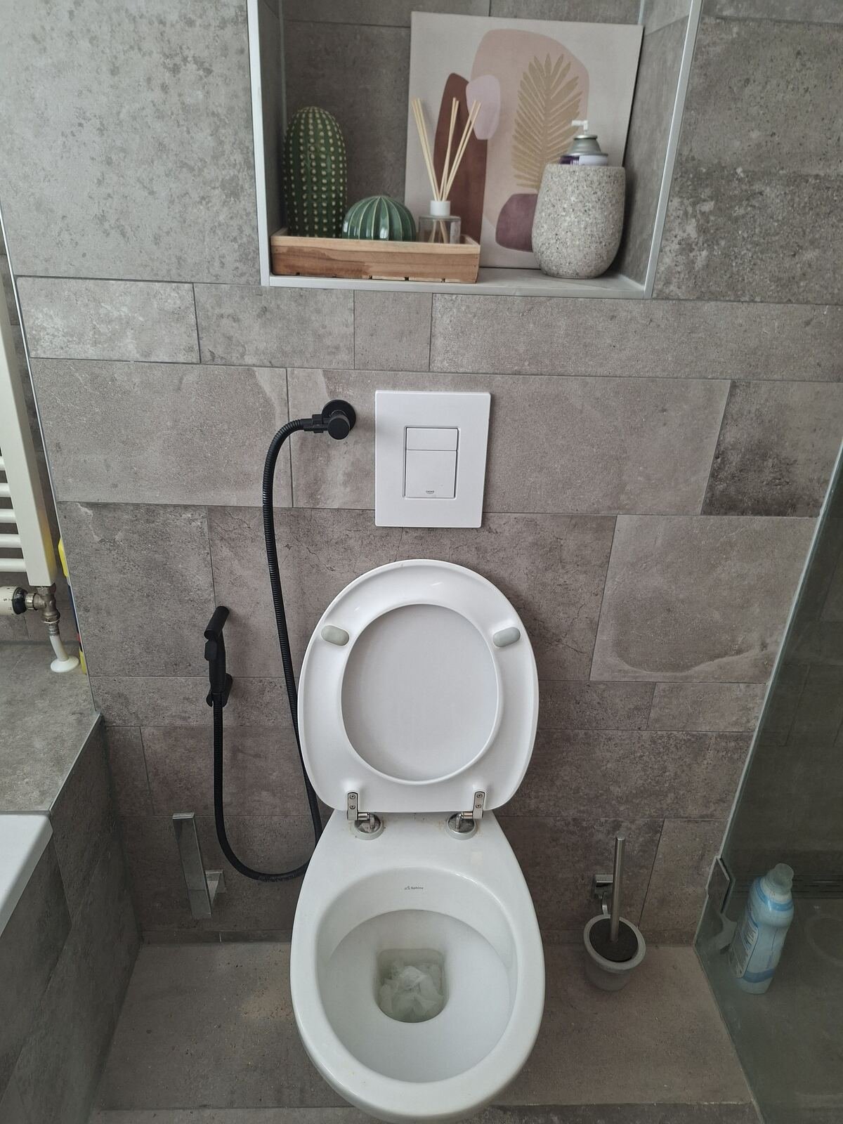 Toilet met zwarte bidetsproeier en Grohe bedieningsplaat in een betegeld toilet